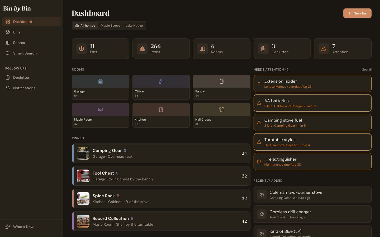 The Bin by Bin web dashboard on a laptop: a row of homes with All homes selected, counts for bins, items and rooms, a grid of rooms, pinned bins, and a Needs attention column listing an overdue loan and low-stock items.